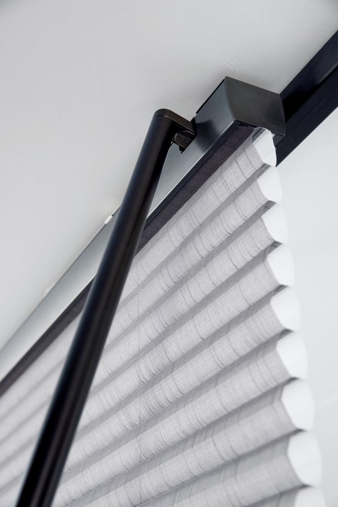 Close-up of the headrail and charging wand on a motorized honeycomb shade
