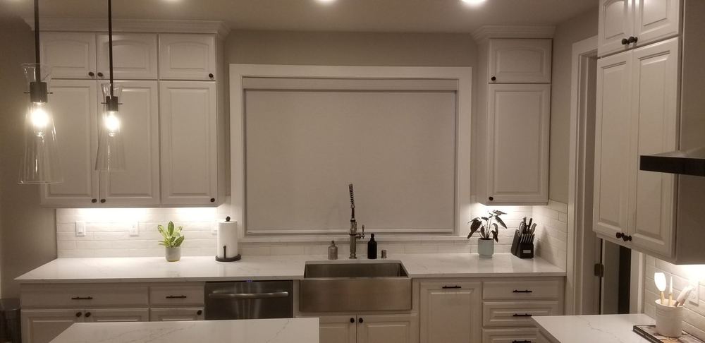 Wide white blackout roller shade lowered over a kitchen sink window