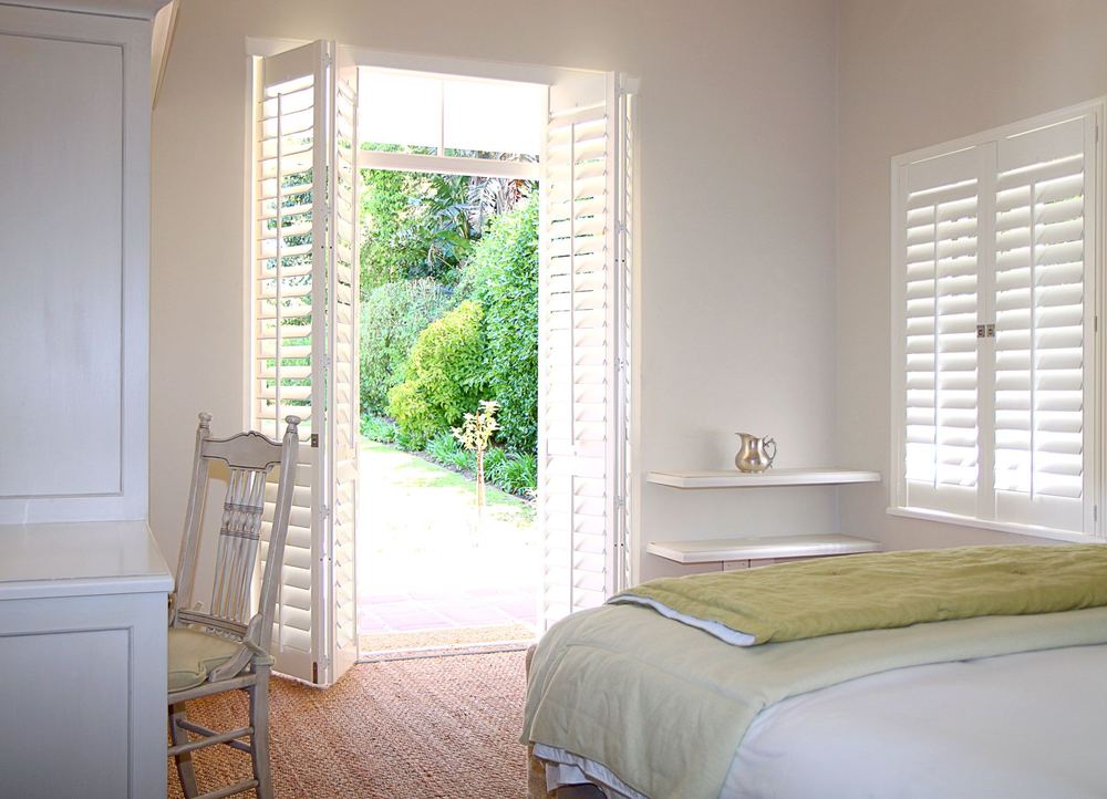 White Woodlore® bi-fold shutter doors opened onto a garden